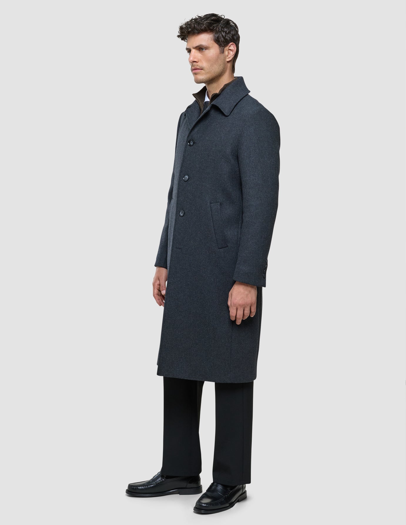 Ein Mann, der einen dunkelgrauen Maxi-Wollmantel im minimalistischen skandinavischen Stil über einem Hemd und einer dunklen Hose trägt.